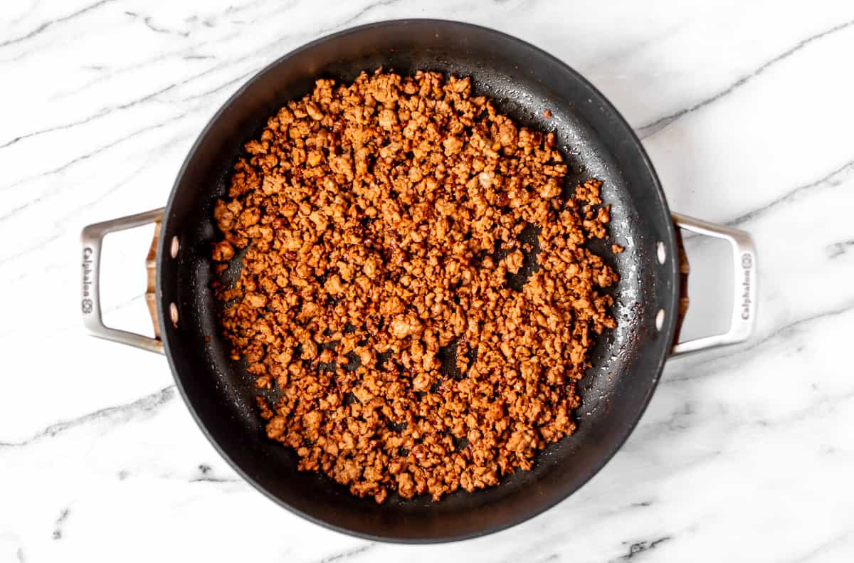 Seasoned cooked ground pork in a black skillet over a marble background.