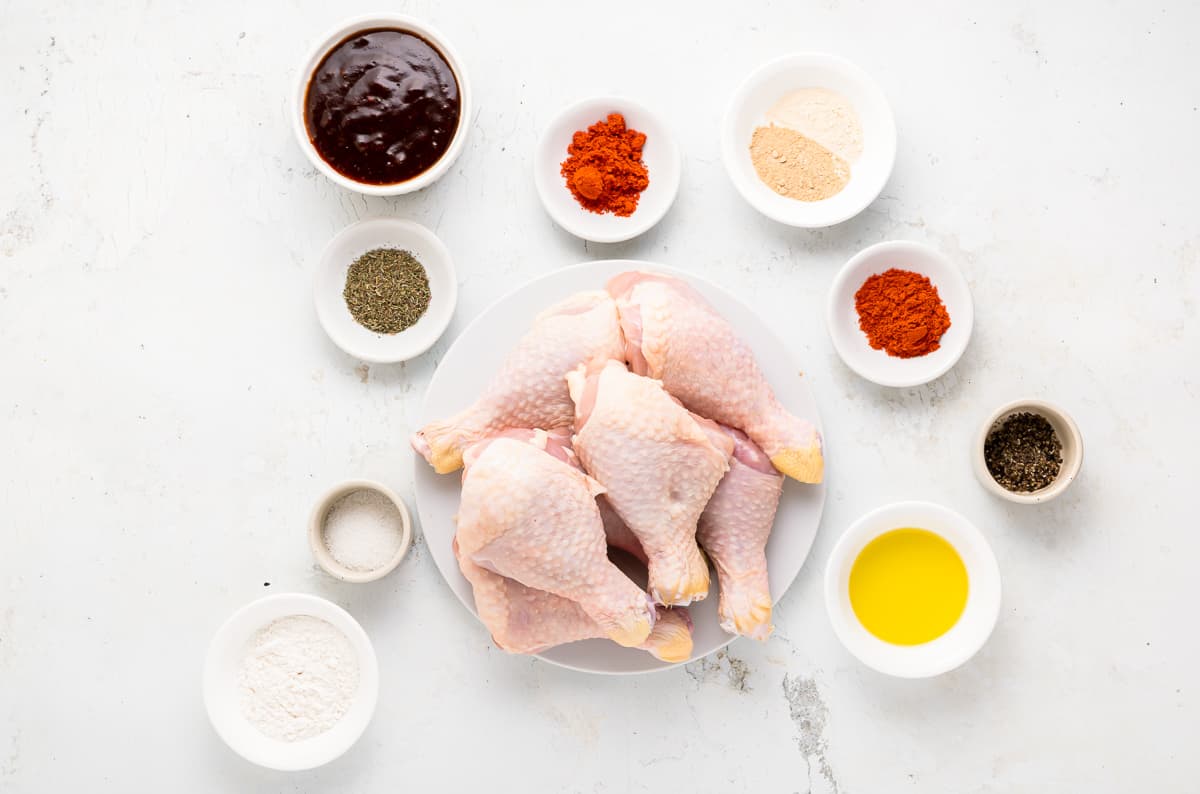 Ingredients needed to make baked BBQ chicken drumsticks on a white background.
