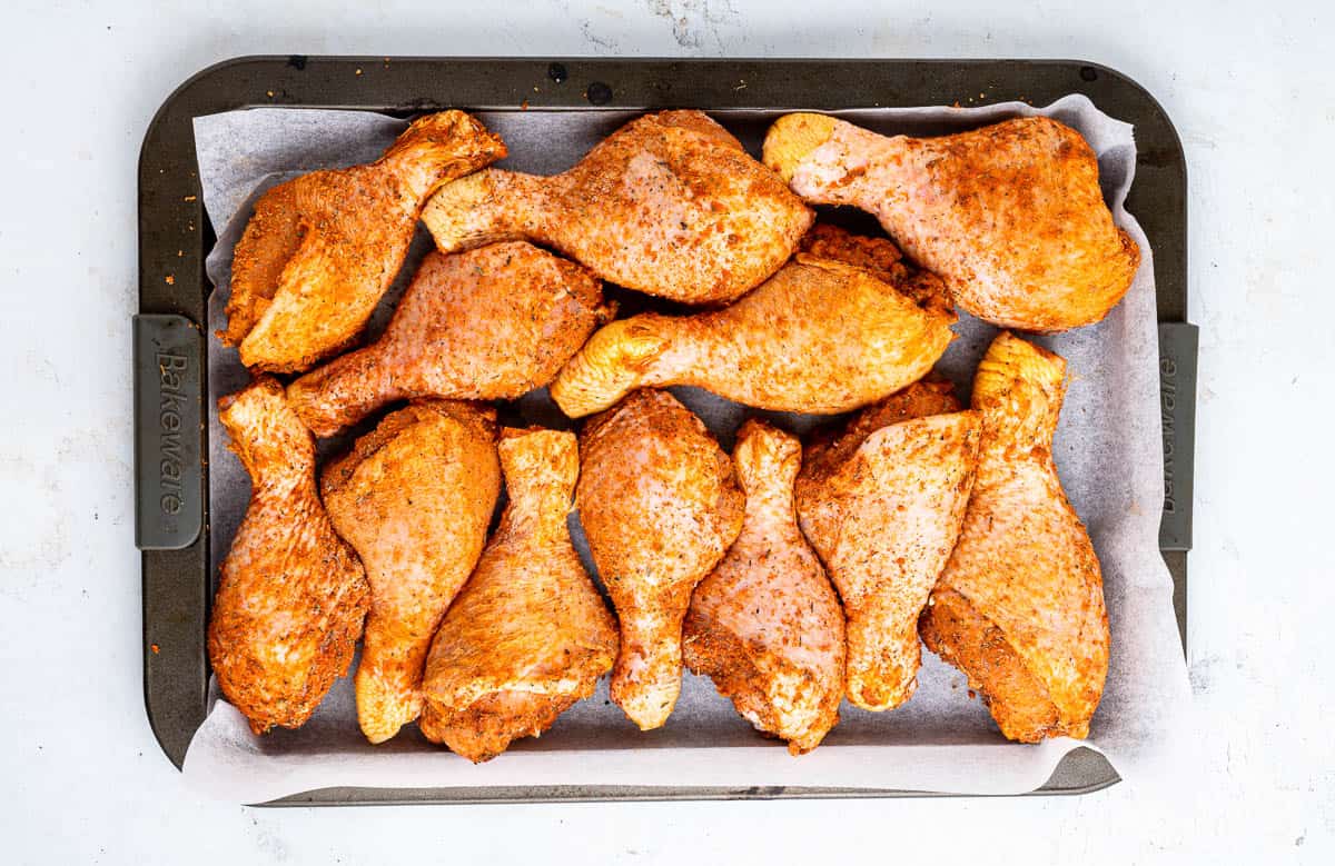 Seasoned chicken drumsticks laid out on a baking sheet.