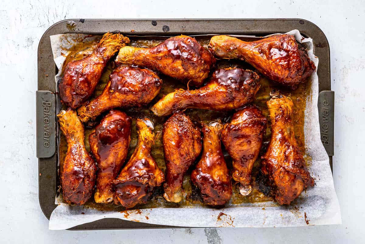 Baked chicken drumsticks coated in barbecue sauce on a sheet pan.