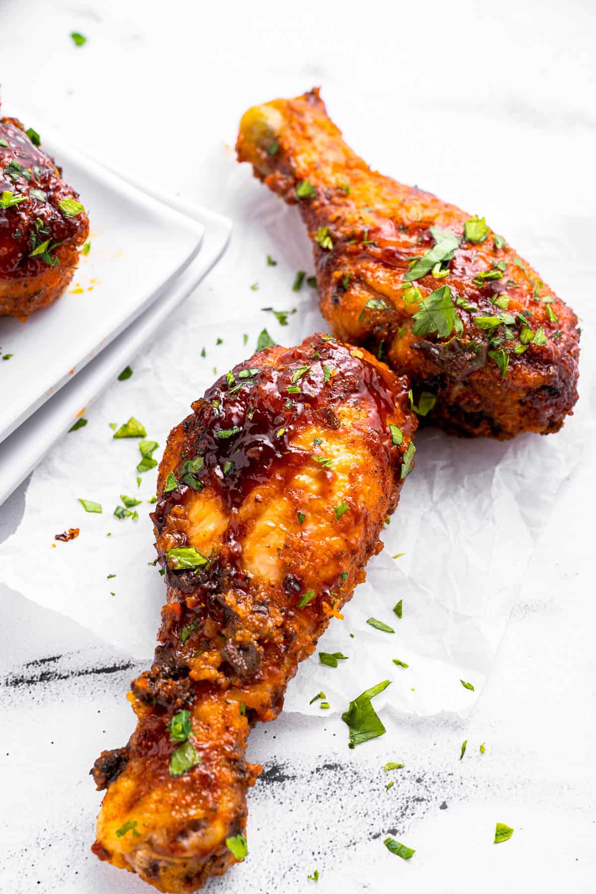 Two baked BBQ chicken drumsticks on a white background.