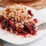 A slice of cherry crumb pie on a white plate with a fork.