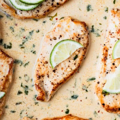 Pan seared chicken breast in a creamy cilantro lime sauce garnished with fresh cilantro and slices of limes.