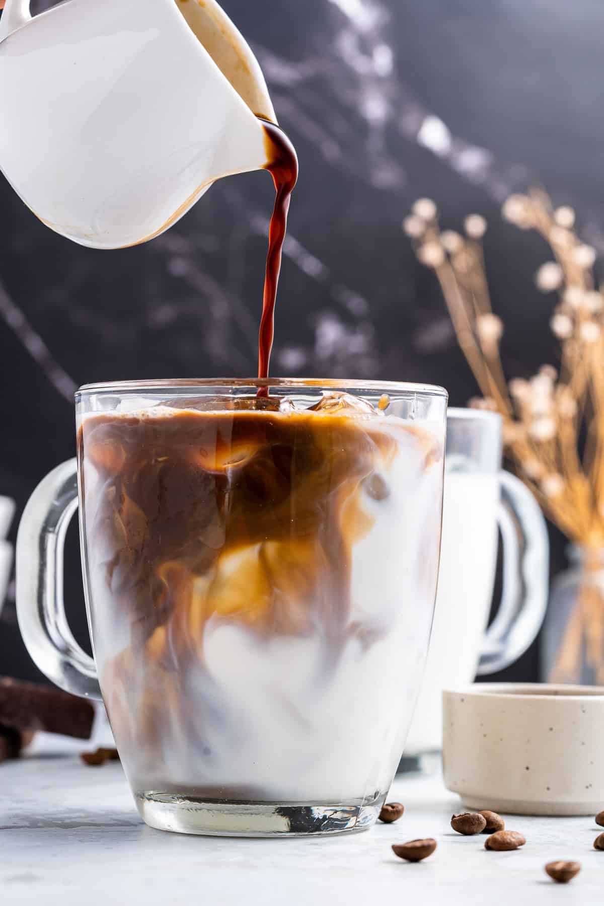 Coffee being poured into a glass of ice and milk.