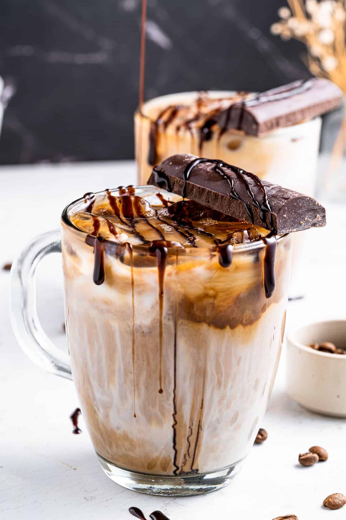 An iced mocha latte in a glass mug with a chocolate bar and chocolate drizzle on top.