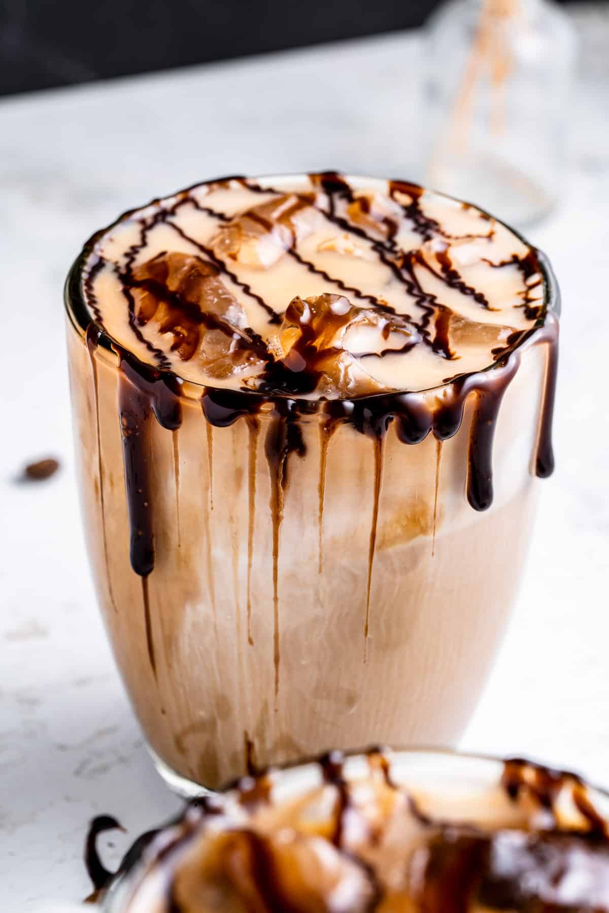 Close up of an ice mocha latte with chocolate drizzle over a white and ray background.