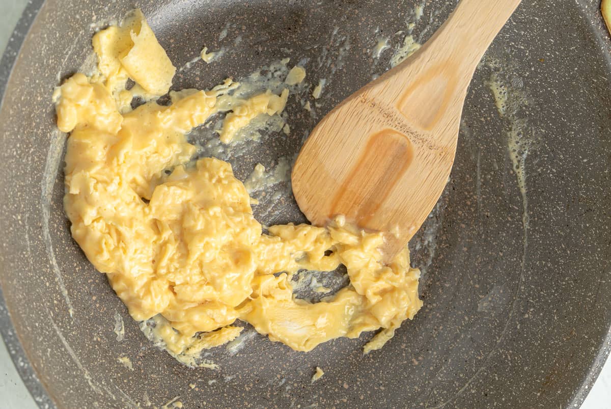 Close up of scrambled eggs in a skillet with a wood spoon.