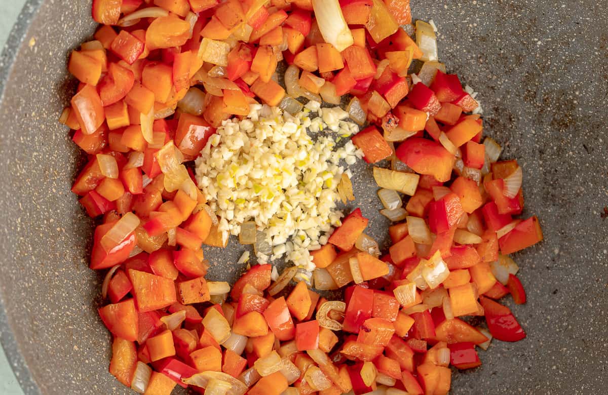Pepper, onion, carrot and garlic cooking in a skillet.