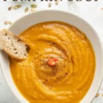 Spicy pumpkin soup in a white bowl with bread and text overlay.