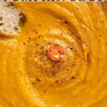Close up of spicy pumpkin soup in a white bowl with bread and text overlay.