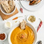 Spicy pumpkin soup in a white bowl with bread in it and other ingredients all around it with text overlay.