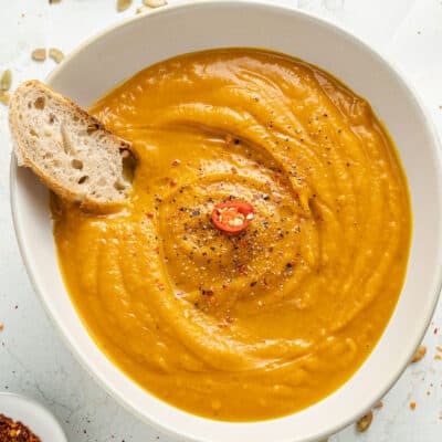 Overhead of a white bowl of spicy pumpkin soup with bread in it.