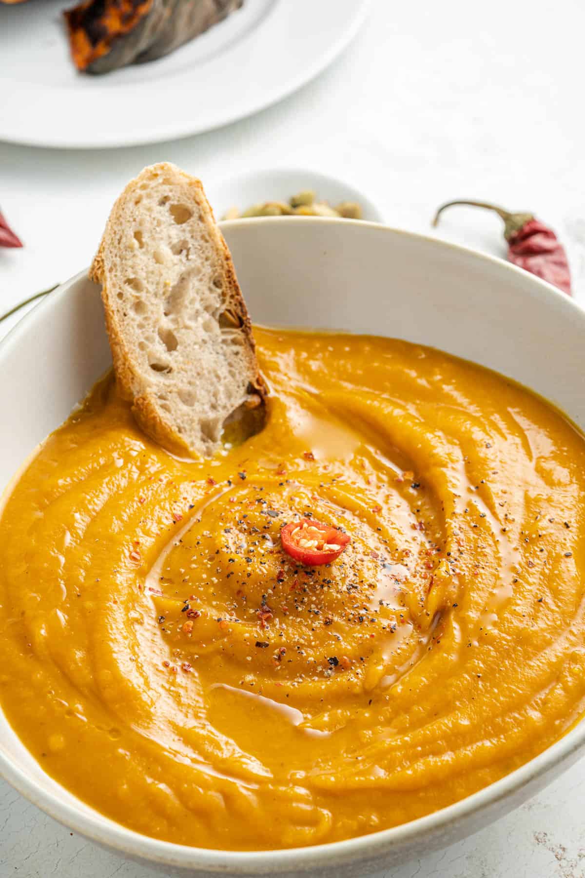 Close up of spicy pumpkin soup in a white bowl with a piece of bread in it.