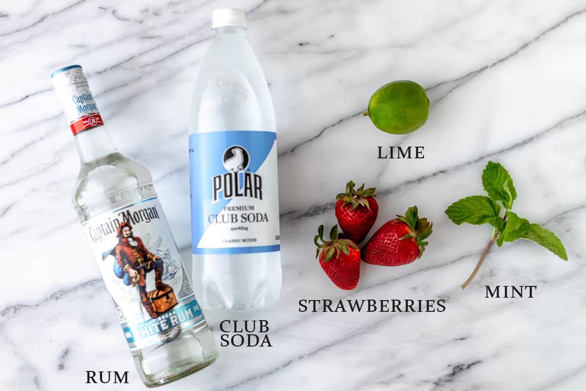 Ingredients needed to make a strawberry mojito on a marble background with text overlay.