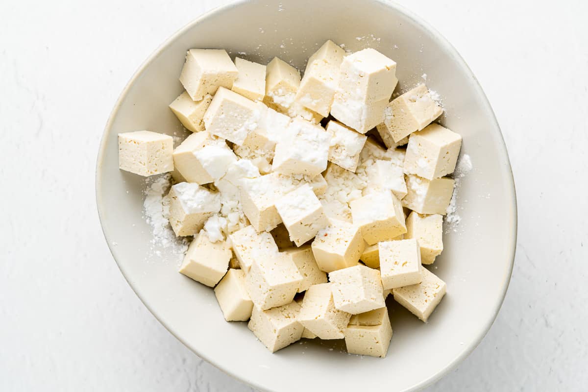 Tofu cubes and cornstarch in a white bowl.