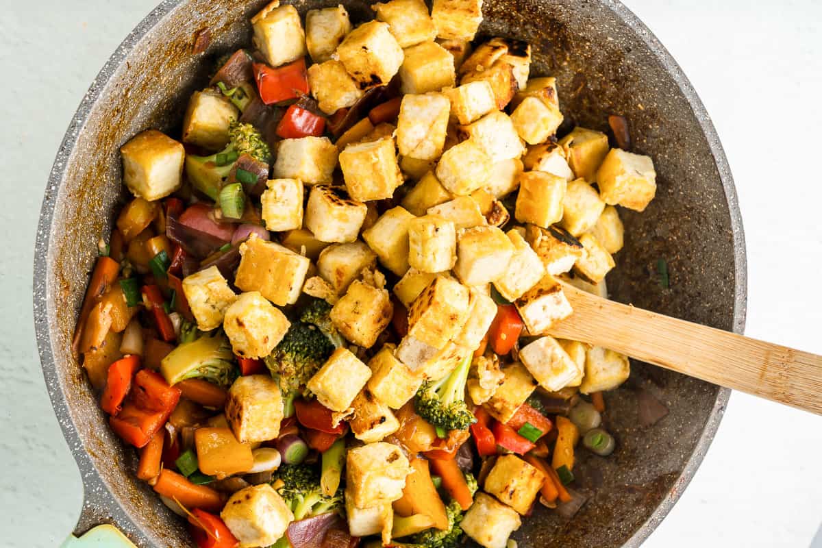 Tofu stir fry in a skillet with a wood spoon.