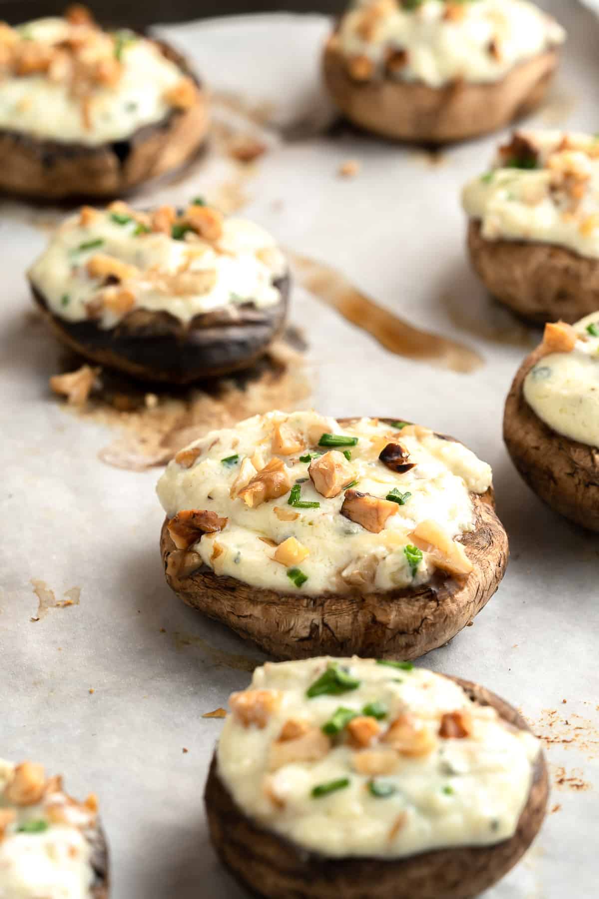 Close up of baked vegetarian stuffed mushrooms on a parchment paper lined baking sheet.