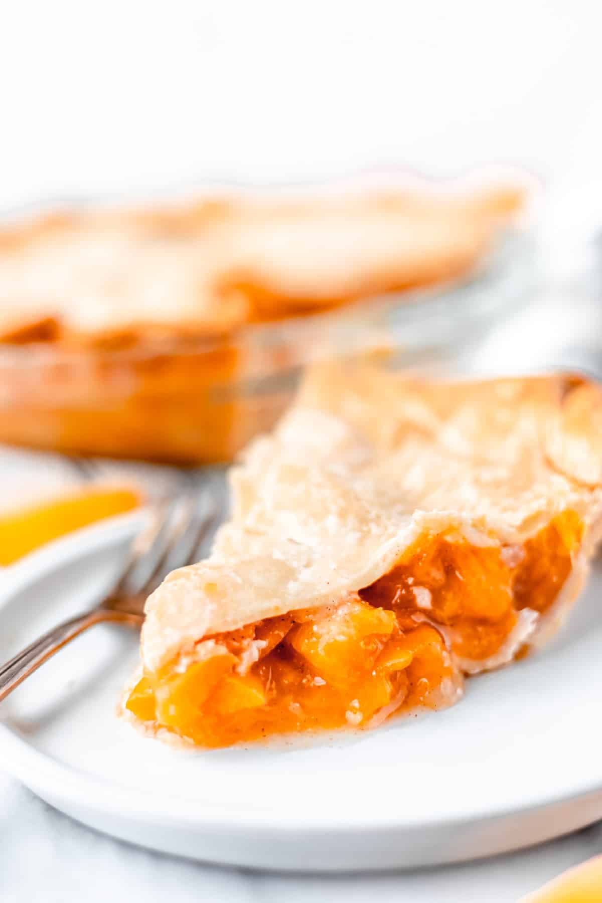 Close up of a slice of apricot pie with the remaining pie in the background.