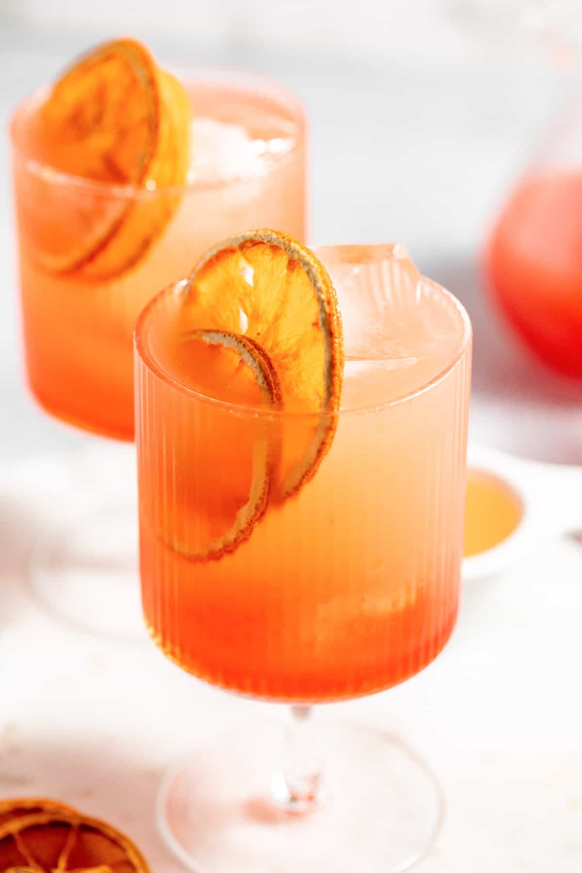 Close up of a blood orange aperol spritz with a second glass and pitcher of juice in the background.