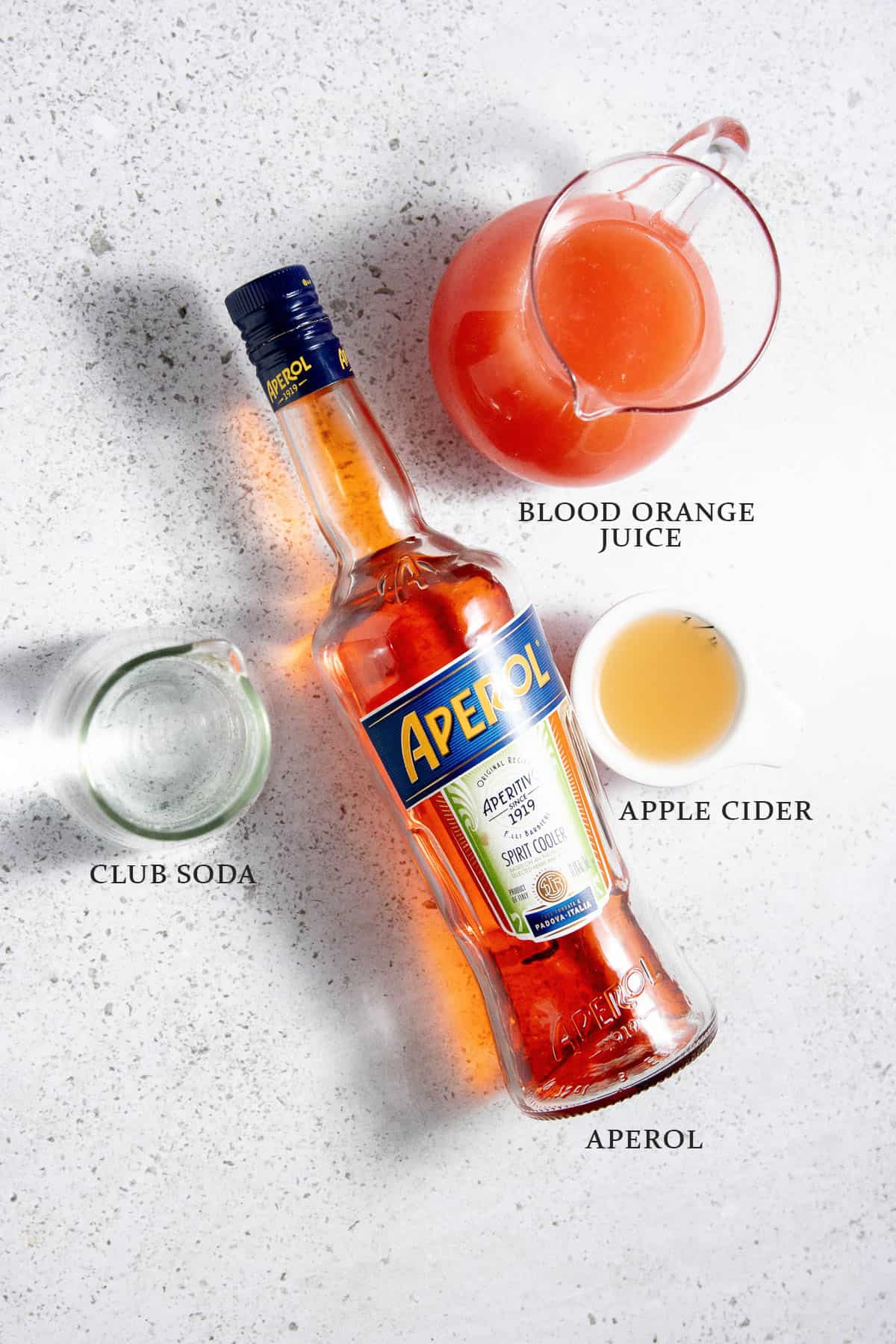 Ingredients to make a blood orange aperol spritz with text overlay.