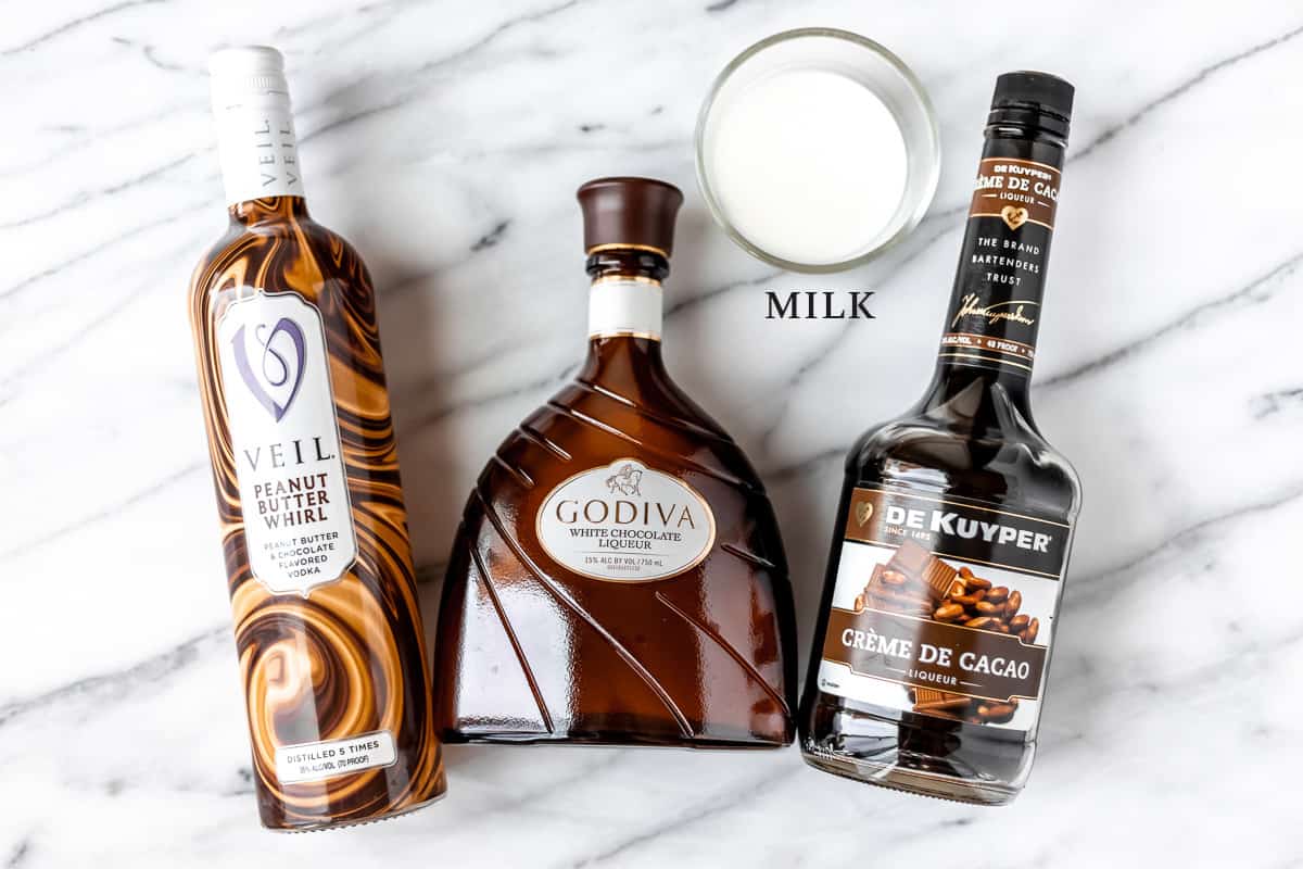 Ingredients needed to make a chocolate peanut butter martini on a marble background.