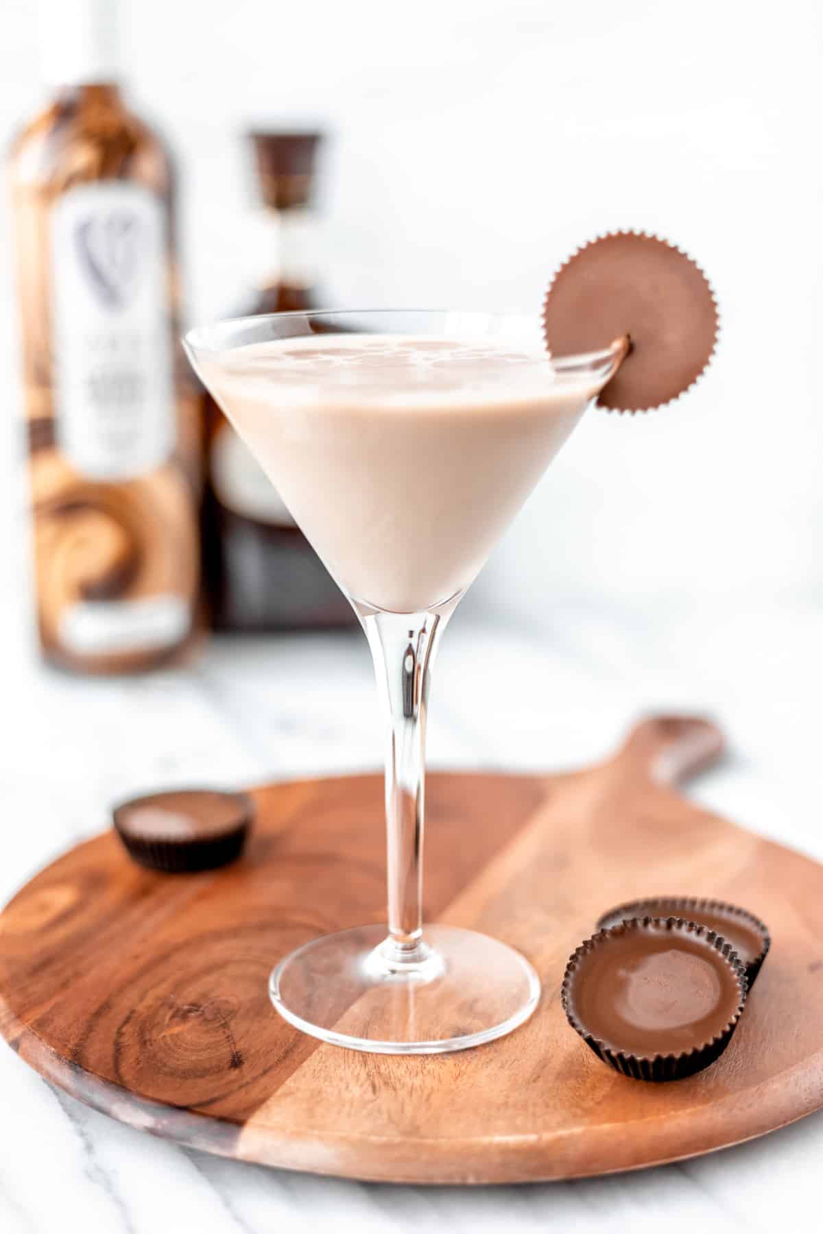 A chocolate peanut butter martini garnished with a Reese's cup and more Reese's cups around it.