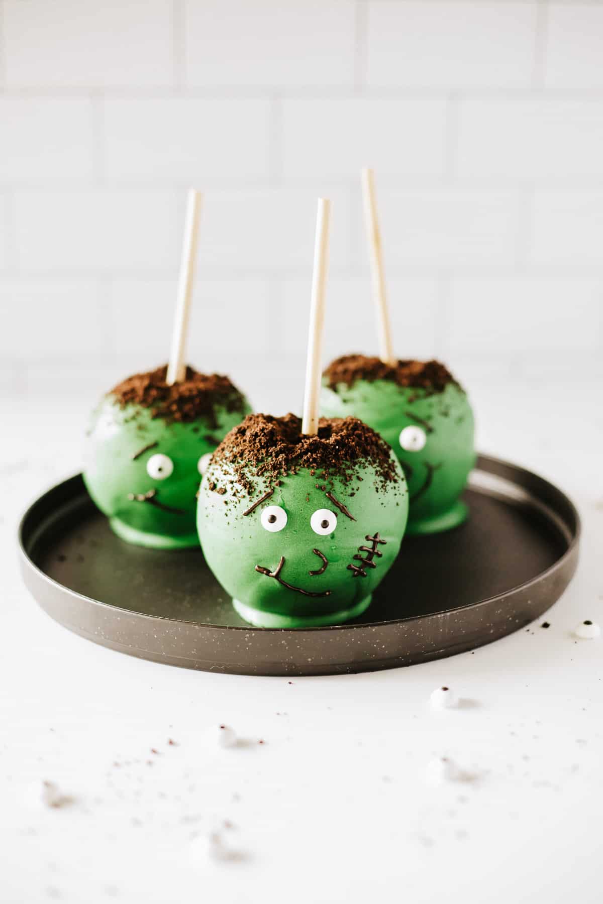 Three Frankenstein candy apples on a black plate over a white background.