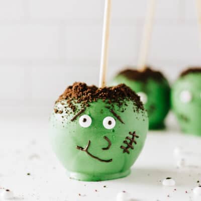 A Frankenstein candy apple on a white background with 2 more blurred in the background.