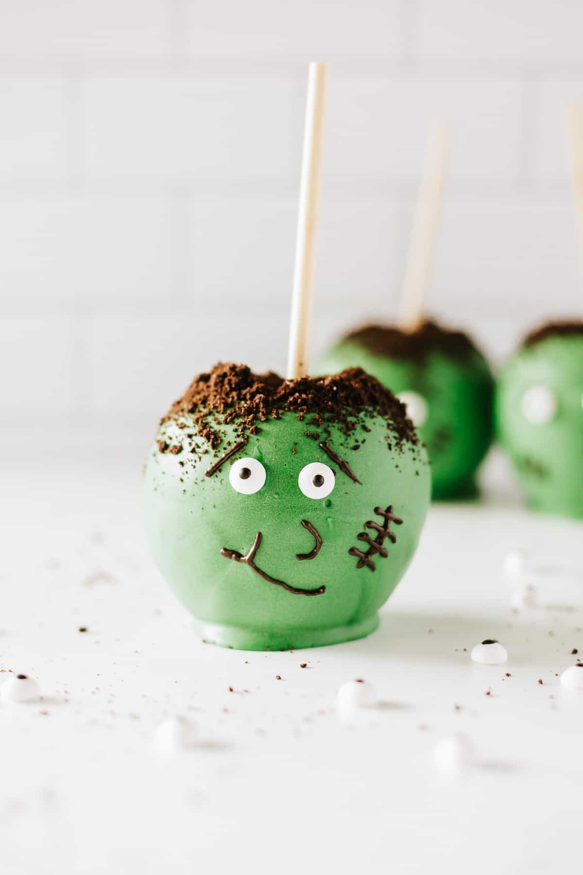 A Frankenstein candy apple on a white background with 2 more blurred in the background.
