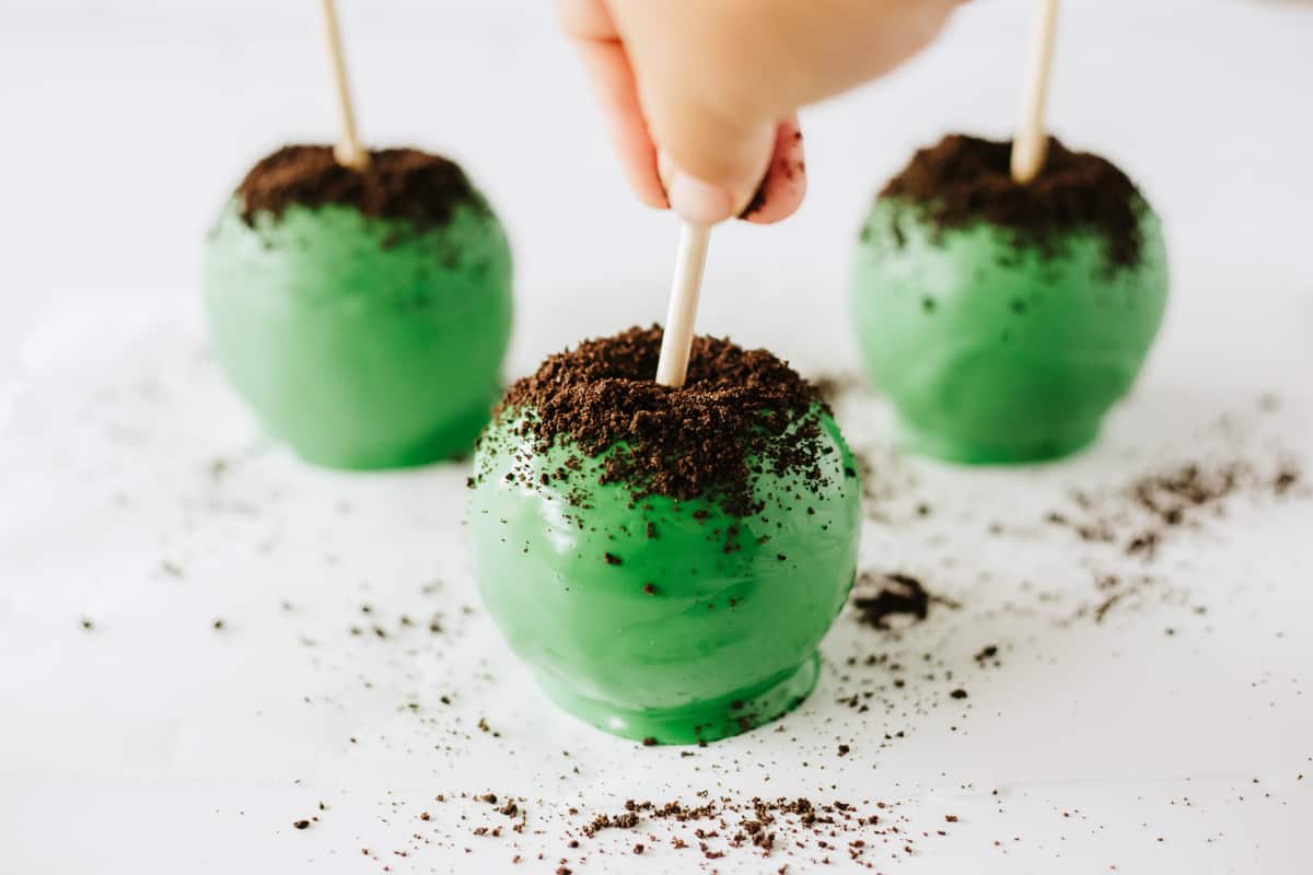 Oreo crumbs being sprinkled on top of a green candy apple.