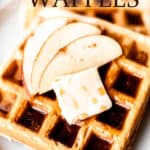 Apple cinnamon waffles on a plate topped with butter, syrup and apple slices with text overlay.