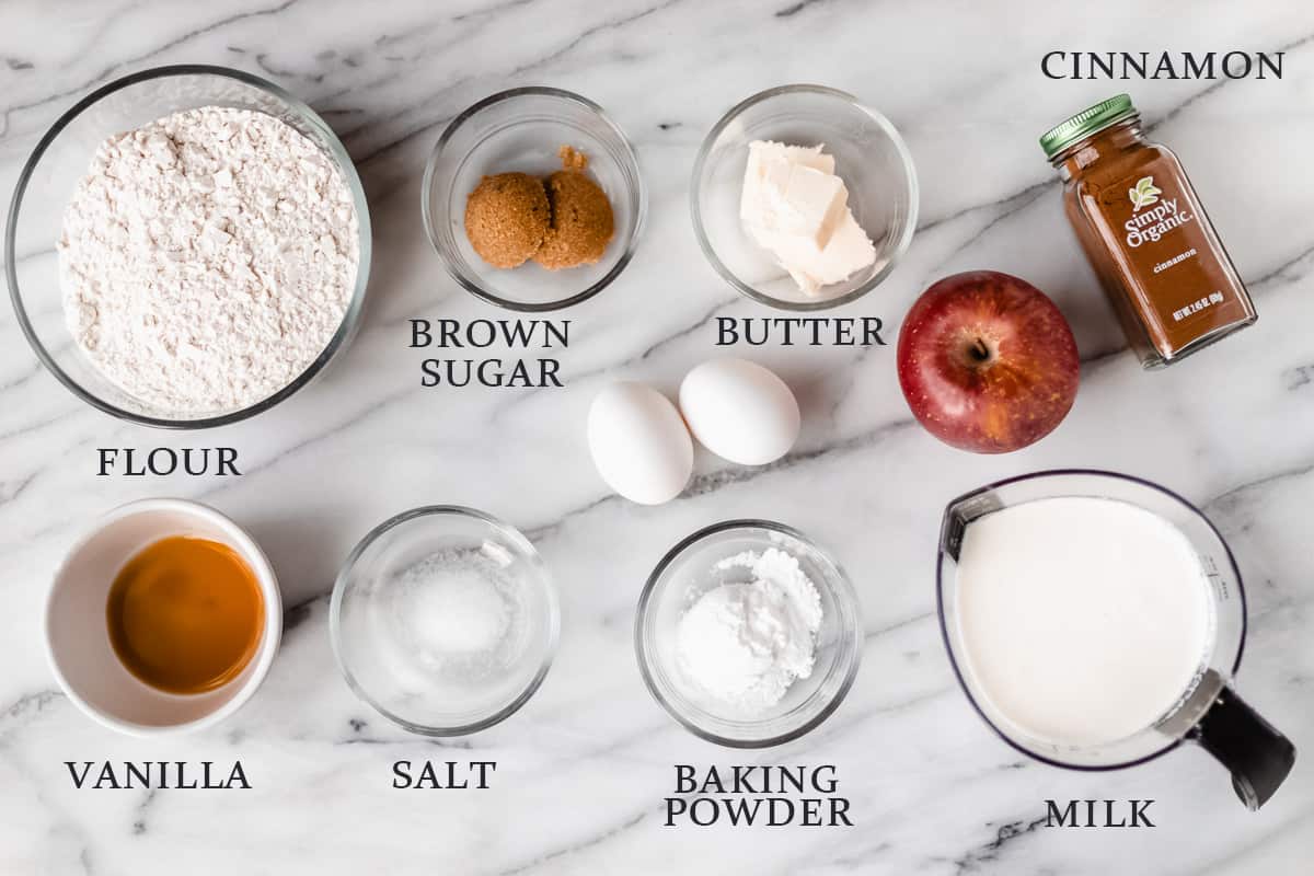 Ingredients needed to make apple cinnamon waffles laid out on a marble background with text overlay.