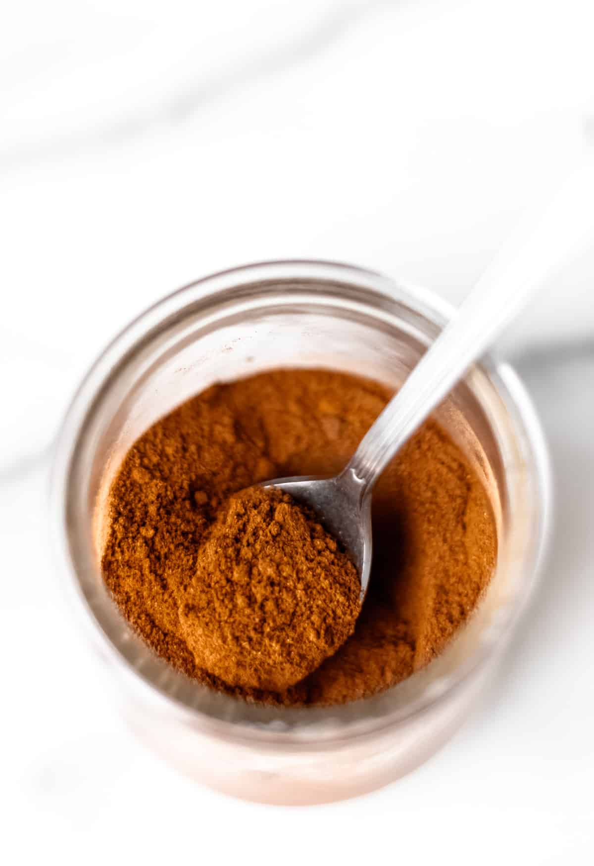 A spoon inside of a glass jar filled with apple pie spice mix.