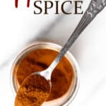 A jar of apple pie spice with a small spoon filled with spice on top of it and text overlay.