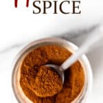 A jar of apple pie spice with a small spoon in it and text overlay.