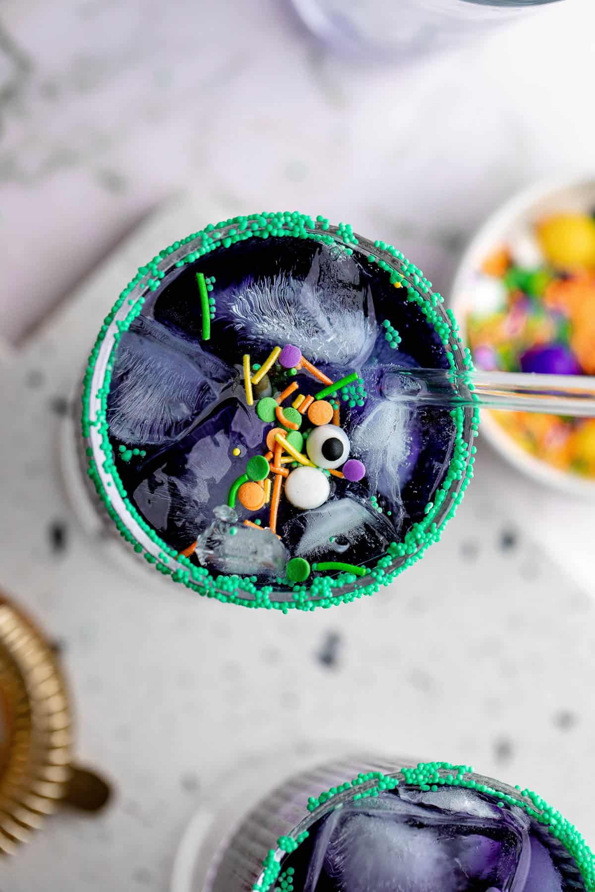 Overhead of a blue curacao Halloween cocktail garnished with sprinkles and candy eyes.