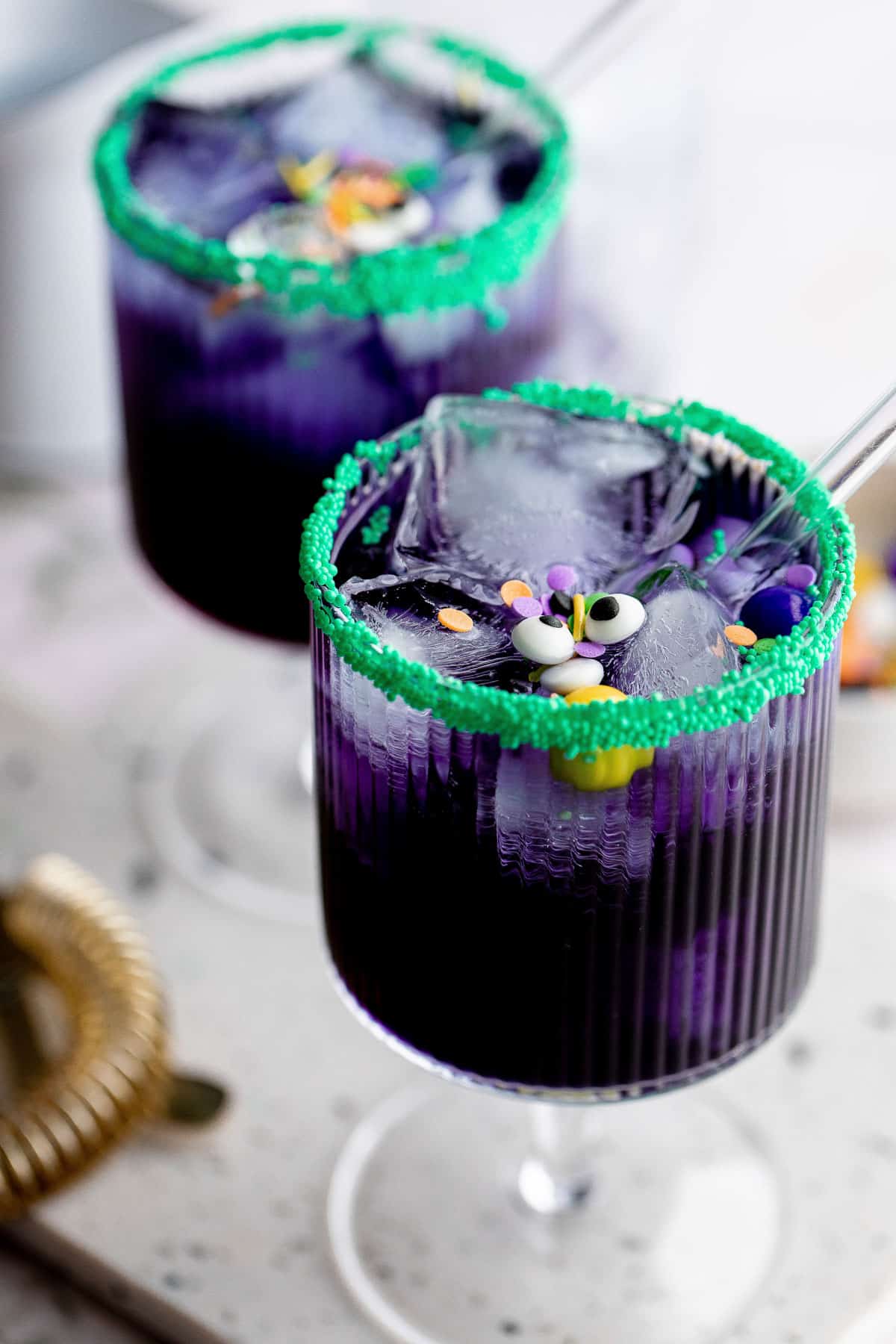 Two blue curacao Halloween cocktails garnished with sprinkles, candy eyes and glass straws.
