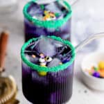 Two blue curacao Halloween cocktails garnished with sprinkles, candy eyes and glass straws with text overlay.
