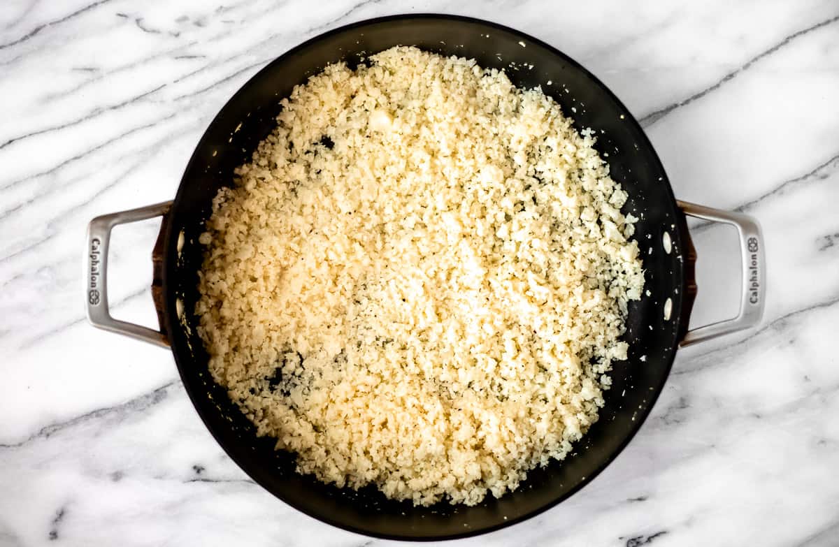 Cooked cauliflower rice in a black skillet.