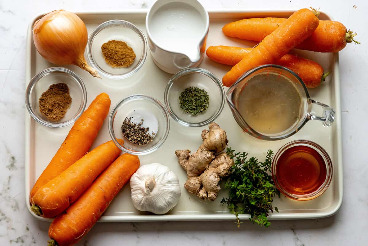 Ingredients needed to make instant pot carrot soup on a baking sheet.