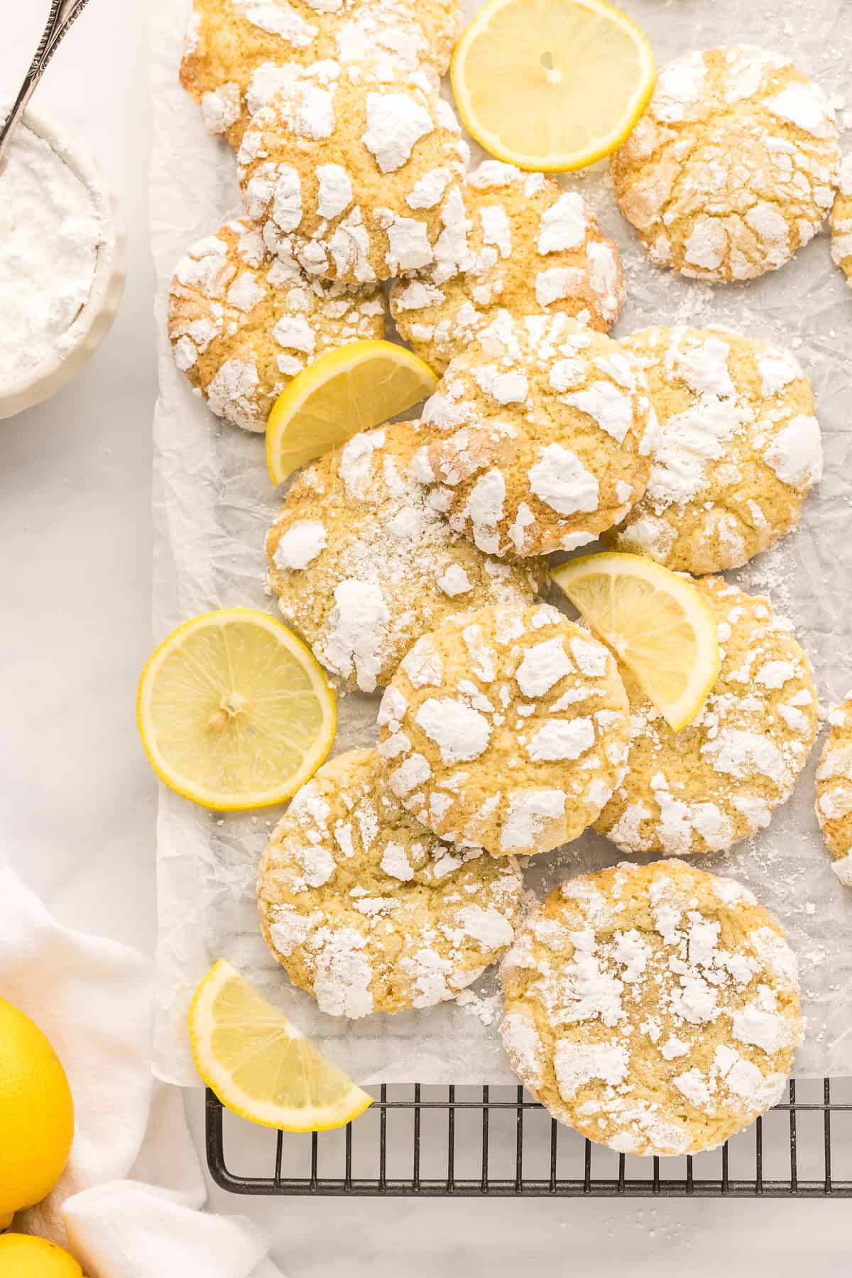 Overhead of lemon crinkle cookies and lemon slices on a parchment paper lined cooling rack.