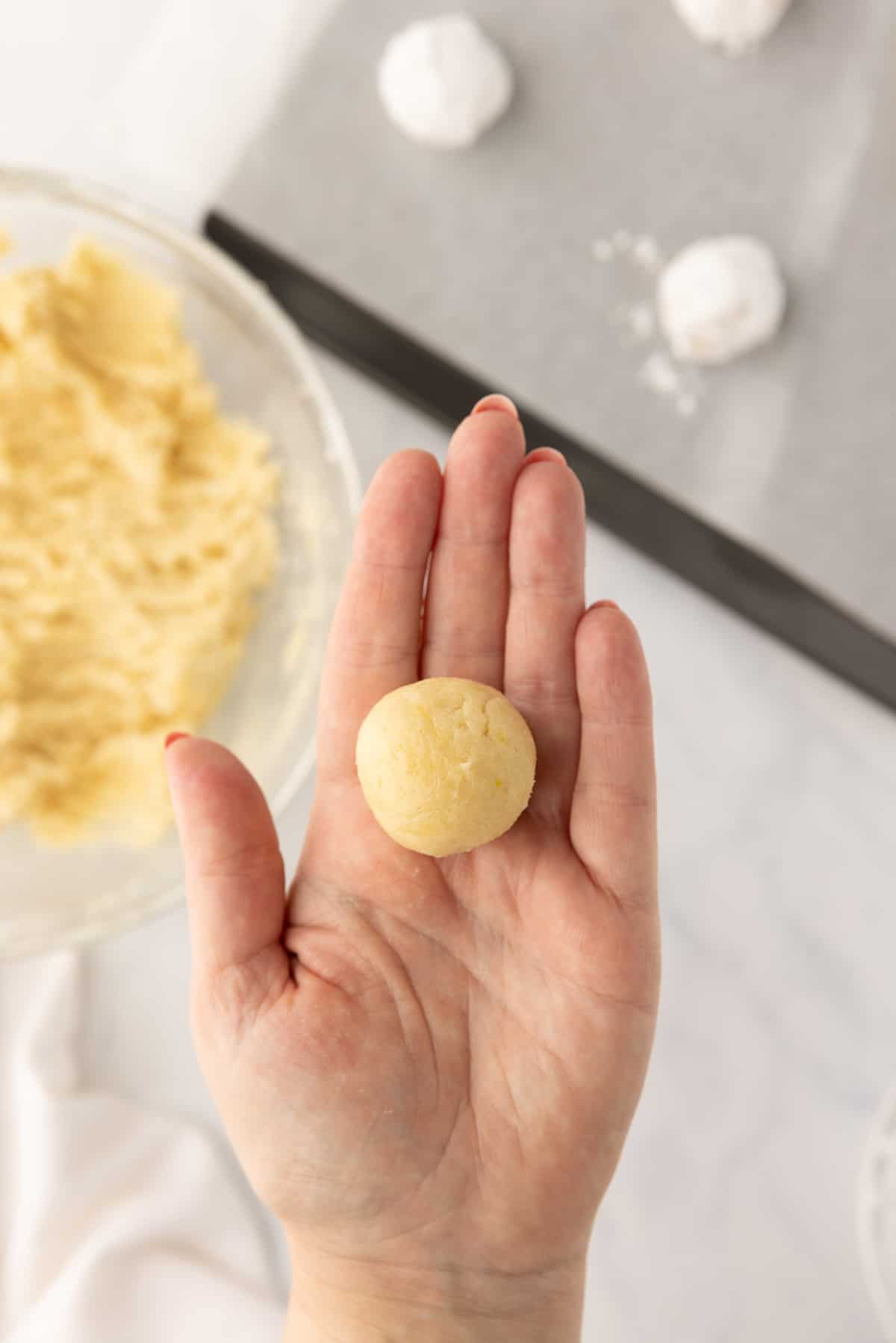 A lemon crinkle cookie dough ball in a hand.