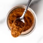 Close up of a spoonful of pumpkin pie spice on top of a glass spice jar.