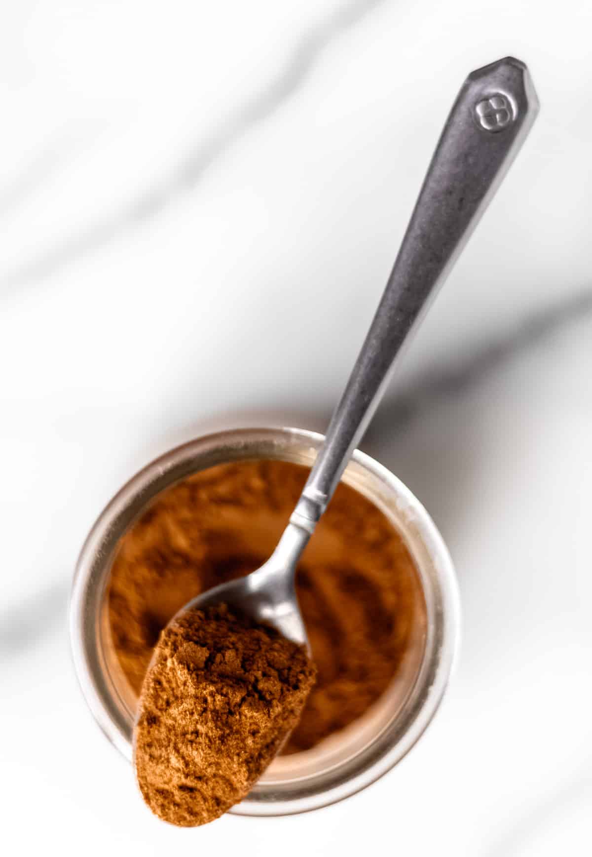 A spoonful of pumpkin pie spice on top of a glass spice jar.