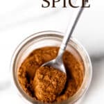 A glass jar of pumpkin pie spice with a small spoon in it and text overlay.