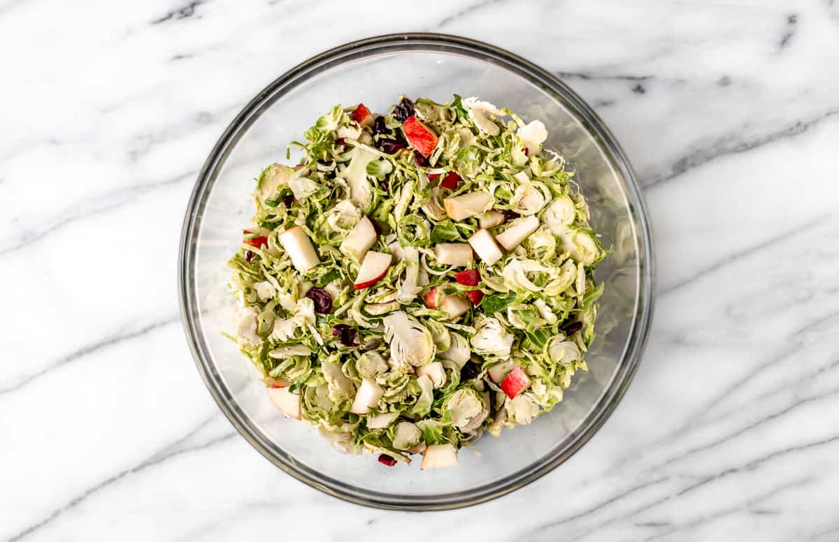 Shaved brussels sprouts salad in a large glass bowl on a marble background.