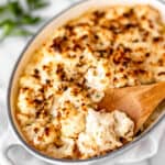 A dish of truffle cauliflower mac and cheese with a wood spoon lifting some up with text overlay.
