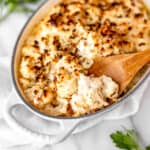 A dish of truffle cauliflower mac and cheese with a wood spoon lifting some up.