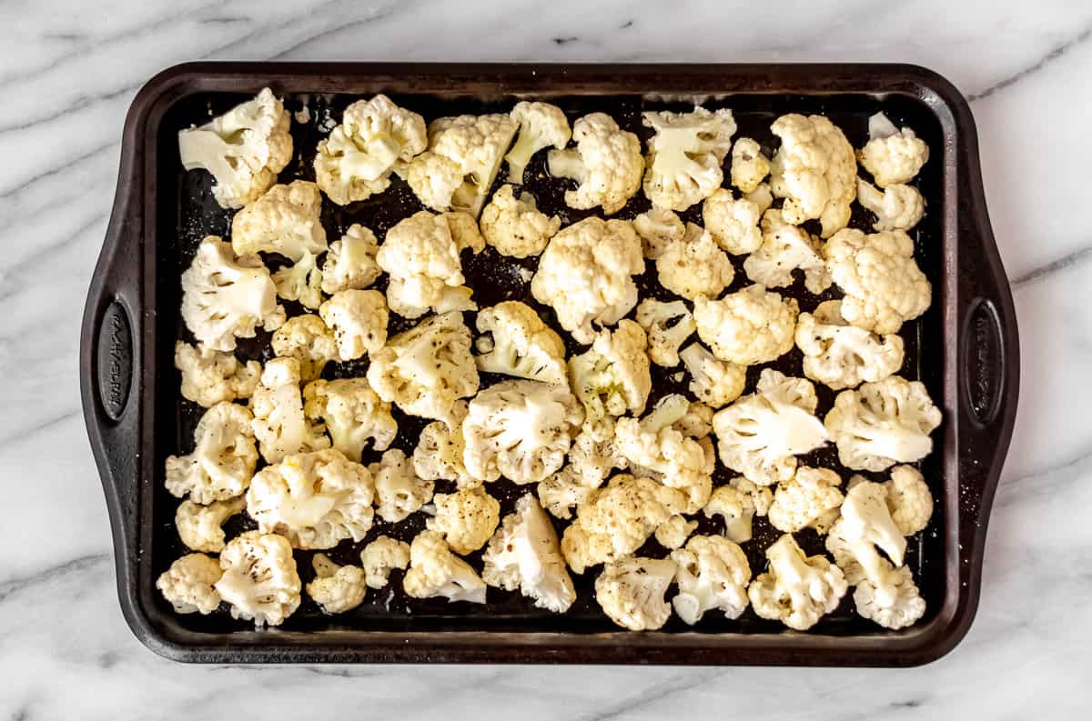 Raw cauliflower drizzled with olive oil and seasoned with salt and pepper on a baking sheet.