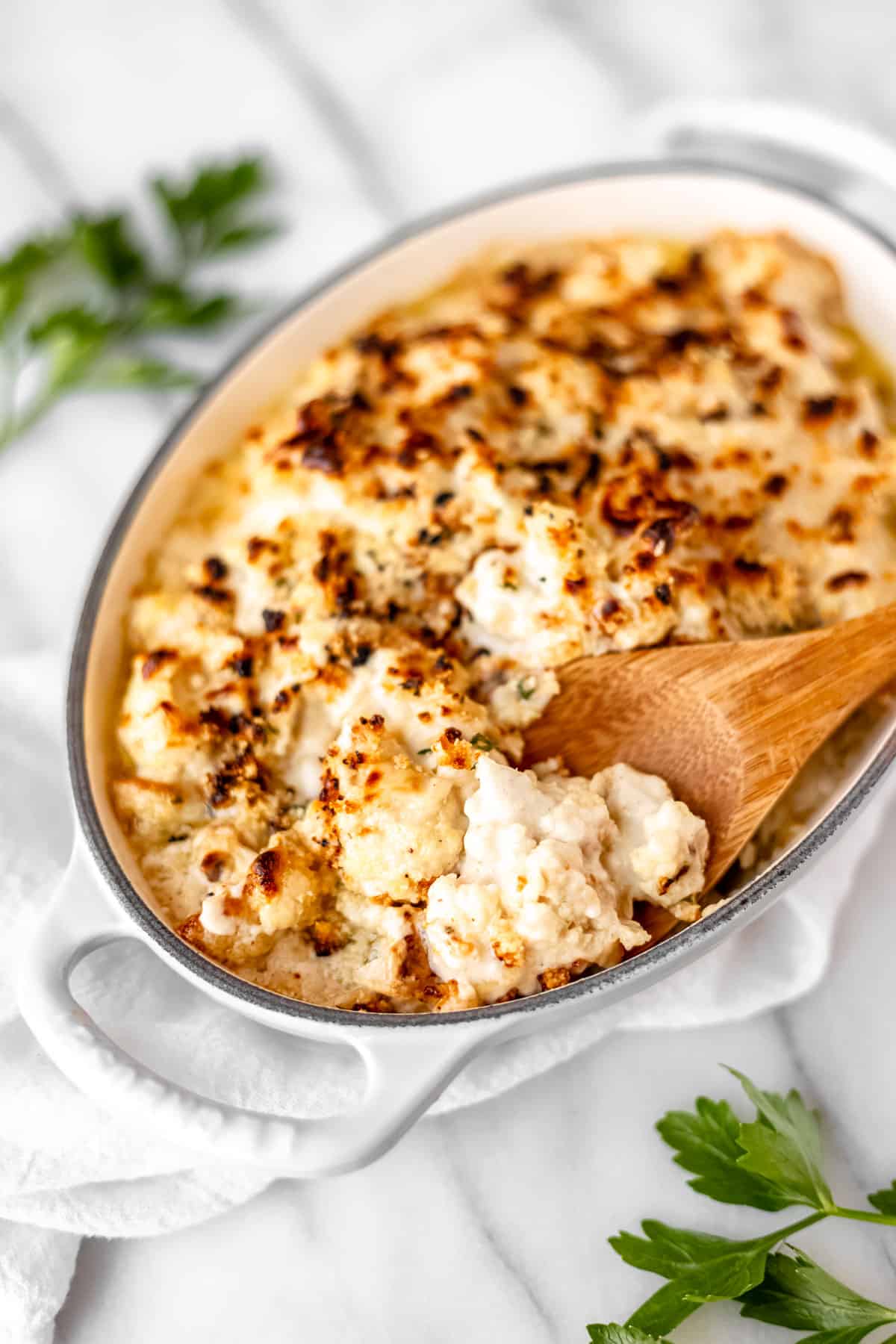 A dish of truffle cauliflower mac and cheese with a wood spoon lifting some up.